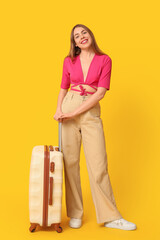 Canvas Print - Happy young woman with suitcase on yellow background