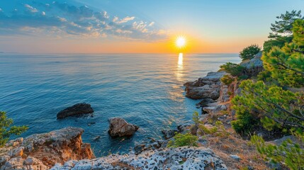 Wall Mural - A beautiful ocean view with a large rock formation in the foreground. The sun is setting in the background, casting a warm glow over the scene