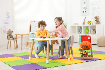 Sticker - Cute little children playing with colorful toy pyramid at white table in kindergarten