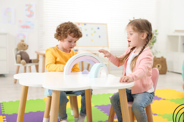 Canvas Print - Cute little children playing with colorful toy rainbow at white table in kindergarten