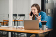© Satori Studio - Smiling businesswoman in blue blazer talking on phone and working on laptop at desk in modern office.