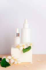 Wall Mural - Cosmetic toner and serum in blank packages on a podium against a white wall background with jasmine flowers. Natural skin care products concept