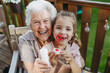 © Halfpoint - Granddaughter blowing bubbles with elderly grandma. Senior lady spending time with young girl, enjoying together time.