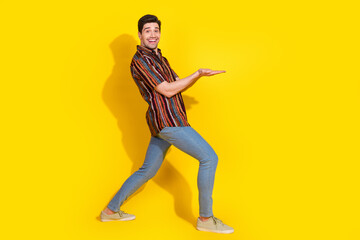 Wall Mural - Full length portrait of nice young man hold empty space wear shirt isolated on yellow color background
