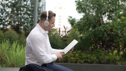 Wall Mural - Businessman wear his headphone to listen relaxed music while take off suit and move to music at green city. Manager with headset dancing movement with lively song while hold phone. Back view. Urbane.