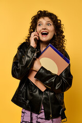 Wall Mural - A young woman with curly hair poses in a black leather jacket against a vibrant yellow background.