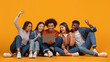 © Prostock-studio - A group of five diverse friends sit on a yellow background, looking at a laptop and celebrating. They appear excited and happy, with smiles on their faces and arms raised in the air