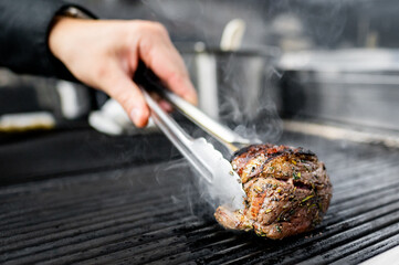 Canvas Print - Close-up of a hand flipping a seasoned steak on a grill, smoke rising.