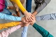 © HendraGalus - Group of people in colorful shirts with hands stacked together in a circle symbolizing teamwork unity and collaboration