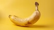 © amorn_m - A single ripe banana with a brown spot, against a yellow background.