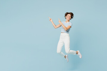Full body young fun woman wears striped t-shirt casual clothes jump high point index finger aside on area mockup isolated on plain pastel light blue cyan background studio portrait. Lifestyle concept.