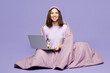 © ViDi Studio - Full body young calm IT woman wear pyjamas jam sleep eye mask rest relax at home sit wrapped blanket work hold use laptop pc computer isolated on plain purple background. Good mood night nap concept.