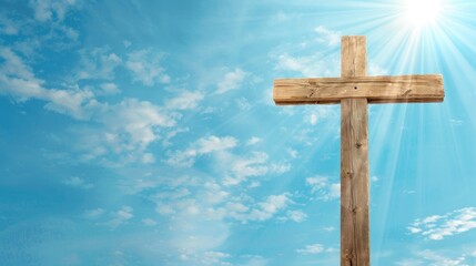 A wooden cross stands tall against a backdrop of a bright blue sky with sun rays shining through the clouds
