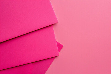 Poster - A flat lay of three pink paper sheets arranged at an angle, creating geometric shapes on the solid color background. The sheets have sharp edges and a glossy finish, adding to their elegance. 