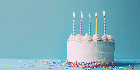 Delicious white birthday cake with five lit candles and colorful sprinkles on a light blue background. Concept of celebration, party, and dessert.