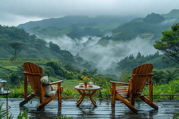 A serene outdoor setting with two wooden chairs and a table on a deck, overlooking misty, green hills and a lush, tranquil landscape