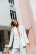 © LIGHTFIELD STUDIOS - A young, beautiful blonde woman in a white suit is gracefully walking down a vibrant Miami street on a sunny day.