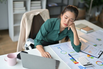 Poster - Young frustrated asian businesswoman feeling tired, exhausted and headache while working with laptop computer and financial graph on desk at office