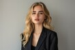 © Elena - Woman With Blonde Hair Wearing a Black Blazer Against a Gray Background