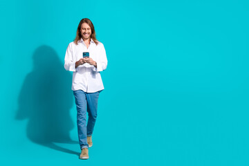 Wall Mural - Full length photo of handsome good mood guy wear white shirt chatting modern gadget walking emtpy space isolated blue color background