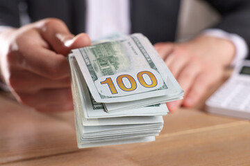 Wall Mural - Money exchange. Man holding dollar banknotes at wooden table, closeup