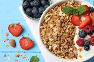 Wall Mural - Tasty granola with berries and yogurt in bowl on light blue wooden table, flat lay