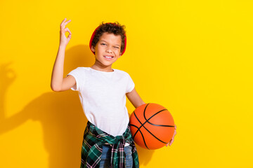 Sticker - Photo portrait of adorable little boy hold basketball ball show okey dressed stylish white garment isolated on yellow color background