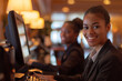 © Tania - Cheerful hotel receptionists collaborating at the front desk, smiling as they work on a computer, with an elegant hotel interior behind them, reflecting a friendly and efficient ho