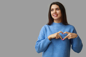 Wall Mural - Beautiful young girl showing heart gesture on grey background. Valentine's Day celebration