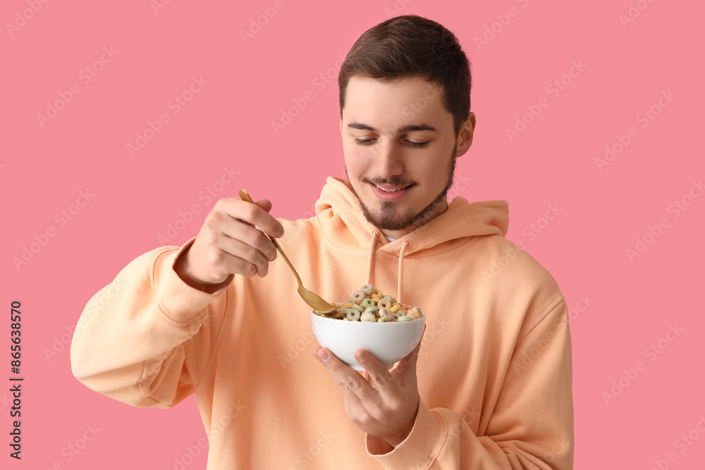 Handsome young man eating tasty cereal rings on pink background