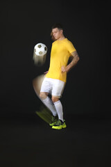 Wall Mural - Young man playing with soccer ball in motion on black background