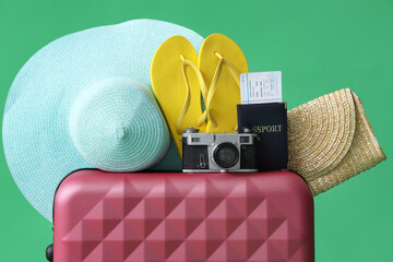 Sticker - Suitcase with beach accessories, passport and photo camera on green background, closeup