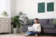 © Pixel-Shot - Young woman in headphones using laptop on floor in living room