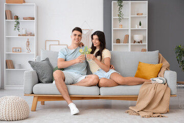 Wall Mural - Happy young couple with glasses of mojito sitting on sofa at home