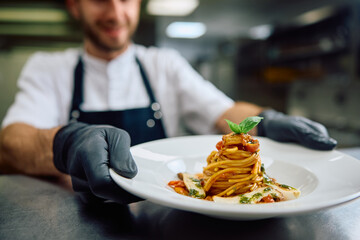 Wall Mural - Close up of professional chef serving pasta while working in  kitchen.