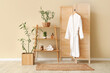 © Pixel-Shot - Folding screen with shelving unit and hanging bathrobe near beige wall