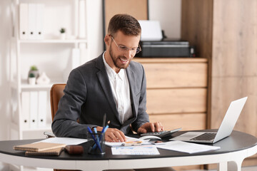 Sticker - Young businessman in eyeglasses working with documents and laptop at workplace in office