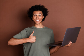 Wall Mural - Photo of young guy in gray t shirt remote working holding laptop using for online business development thumb up isolated on brown color background