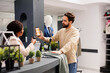 © DC Studio - African American woman cashier scanning Black Friday mobile promo code from customer smartphone, using barcode scanner. Young man shopper using coupon to get discount while shopping in clothing store