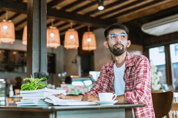 Portrait of a bearded Asian man wearing glasses. Drinking coffee and reading at a coffee shop