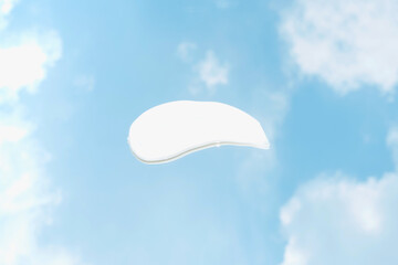 Smear of moisturizing cream against background of sky and clouds, top view.