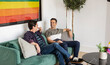 © PintoArt - Two Men Chatting on a Sofa with Pride Flag in Background