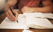 © Stratford/peopleimages.com - Student, hand and writing in notebook at desk for studying, learning or assignment deadline in library. University, education and person with pen for knowledge, scholarship or working on thesis
