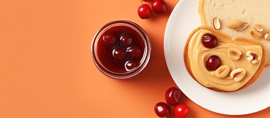 Poster - Top-down view of a peanut butter jar on a white plate, accompanied by cookies, buttered bread, cherries, and peanuts on a vibrant orange backdrop, offering copy space for an image.