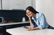 © SHOTPRIME STUDIO - Young woman sitting on kitchen counter talking on cell phone while looking at screen and smiling