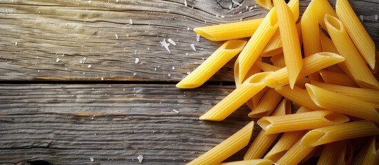 Poster - Close-up photo of vibrant uncooked penne pasta on a wooden table creates a textured Italian food background, perfect for text insertion in the image. Copy space image