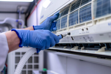 A technician wearing blue gloves is cleaning the air conditioner with tools