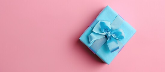 Wall Mural - A small gift box wrapped in blue paper sits on a pink pastel background, illustrating a romantic celebration concept with copy space for images.