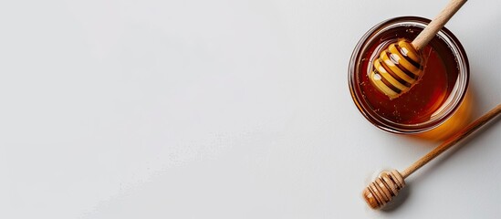 Poster - Delicious honey jar with a wooden honey dipper arranged on a white background providing a top view with copy space image.