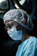 © Seventyfour - Vertical profile view portrait of mature woman as female surgeon performing operation in blue light
